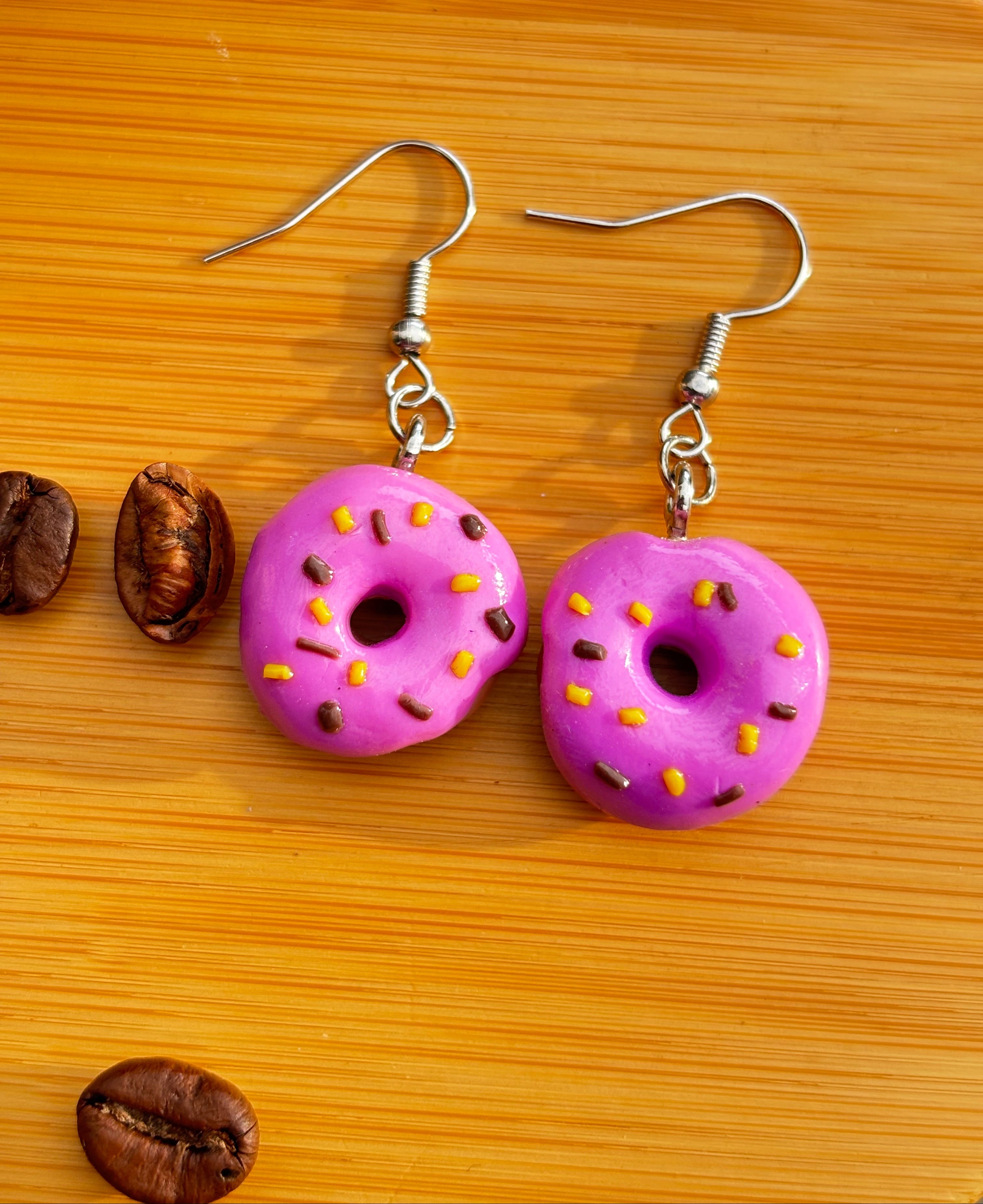 Handgefertigte lila Donut Ohrringe Polymer Clay auf Holzuntergrund mit Kaffeebohnen