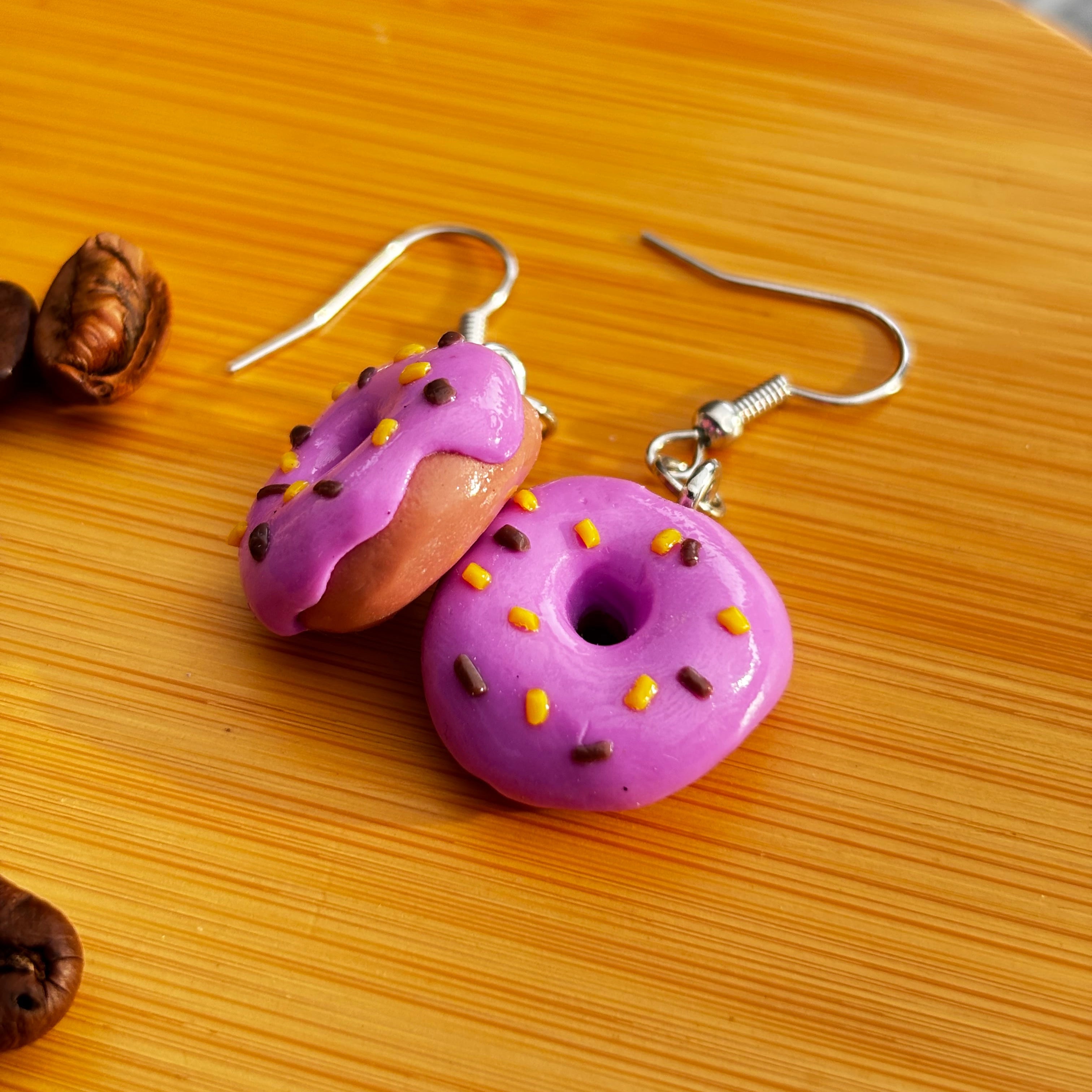 Handgefertigte lila Donut Ohrringe Polymer Clay auf Holzuntergrund mit Kaffeebohnen